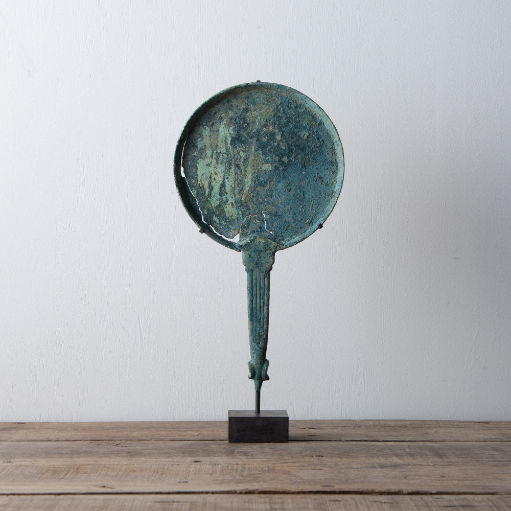 Scythian Bronze Mirror – No.111
黒海北岸 , 紀元前6 - 5世紀
スキタイの羊形鏡（紀元前6 - 5世紀　黒海北岸）
柄の先端に羊の頭が象られた鏡。黒海北岸のギリシア都市オルビアで作られていたと考えられています。ひび割れしていますが、欠損や補修はありません。鏡面側は青い緑青で覆われています。ここまで色濃い緑青が厚く残っているものは古代青銅製品全般でも多くはありません。大抵の場合、土を除去する際に剥がれてしまうか、どこかの時点で持ち主が綺麗にクリーニングしてしまうためです。
