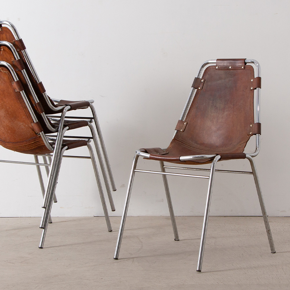 Les arcs Chair in Leather and Steel by Charlotte Perriand
France , 1960s
フランスのスキーリゾート Les arcs（レ・ザルク）の為、1967年に Charlotte Perriand（シャルロット・ペリアン）によってセレクトされたレザーチェア。イタリアの家具メーカーにて製作されたと言われるこちらのチェアは一般に向け販売されることは無く、レ・ザルク　スキーリゾートのみで使われていました。
ペリアンはレ・ザルクの開発計画に参画、施設の設計や内装などトータルにプロデュースしました。
スチールパイプを曲げた簡素なフレームにホワイトステッチが施された頑丈なレザーシートをリベットで固定。腰掛けるとレザーシートがフレームに吊り下がるシンプルでありながら特徴あるデザイン・構造、軽量でスタッキング可能な機能性と利便性が魅力的な一脚です。
