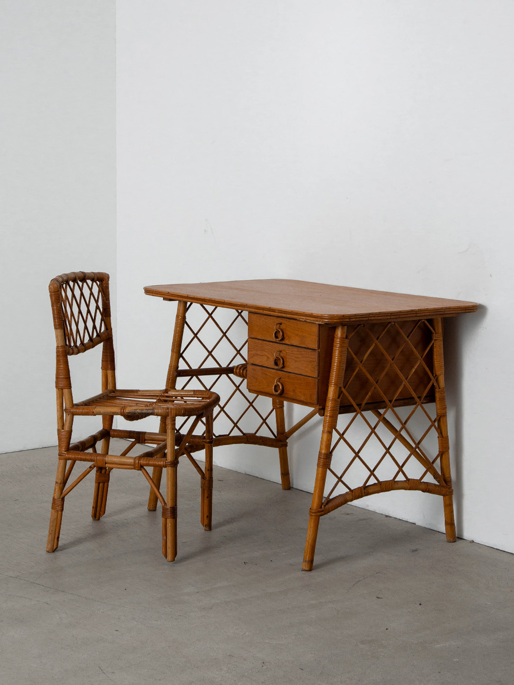 Desk and Chair Set by Louis Sognot in Rattan , Bamboo and Wood
France , 1960s
フランスのデザイナー Louis Sognot（ルイ・ソニョ）によってデザインされたラタンデスクとチェアセット。
格子状に編まれたラタンがデスクサイドに軽やかさとリズムをもたらし、温かみのあるバンブーフレームとの調和が美しい作品。
バンブーリングがついた印象的な3つの引き出しは、十分な収納力を有しています。
