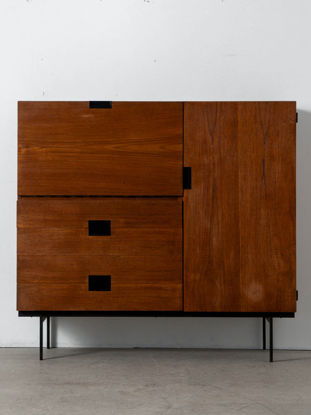 ‘CU01’ Cabinet By Cees Braakman for Pastoe in Teak and Steel
Netherlands , 1950s
オランダのデザイナー Cees Braakman（ケース・ブラークマン）によって、Pastoe（パストー）社のために1958年にデザインされた 'CU01' キャビネット。
'U+N Series' として多彩なバリエーションで展開され、後に 'Japanese Series' とも称される代表的なモデルのひとつ。 日本の美学に着想を得たミニマルな構成が際立ち、シリーズを象徴するハンドルディテール、深みのあるチーク材、そして緻密に計算されたプロポーションとコンポジションが見事に調和しています。
パストー社のディレクター兼デザイナーを務めていたブラークマンの理念を明確に体現するデザインです。
