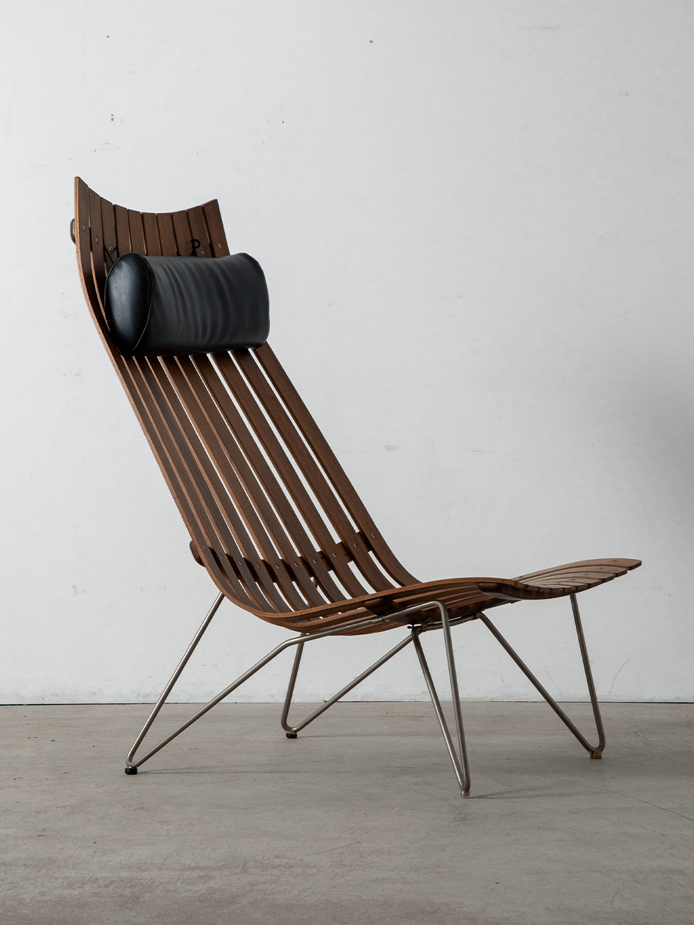 ‘Scandia’ Lounge Chair by Hans Brattrud for Hovik Mobler in Teak , Leather and Steel
Norway , 1960s
ノルウェーのデザイナー Hans Brattrud（ハンス・ブラットルッド）によって、1959年に同国の Hovik Mobler（ホーブ・モブラー）社のためにデザインされた 'Scandia' ラウンジチェア。
木製スラットによってストライプ状に構成されたフレームは、軽やかさと立体的なプロポーションを生み出し、快適な座り心地を実現します。経年したチーク材の風合いとスチールの組み合わせがモダンな印象を引き立て、上質なレザーヘッドレストが機能性を高めます。
1957年、ブラットルッドは大学在学中のプロジェクトとして 'Scandia Junior’ チェアをデザイン。その後 'Scandia’ シリーズの一環としてラウンジチェアがデザインされました。そのデザイン性と機能性は国際的に高く評価され、多くの賞を受賞。北欧デザイン史を象徴する作品として知られています。
