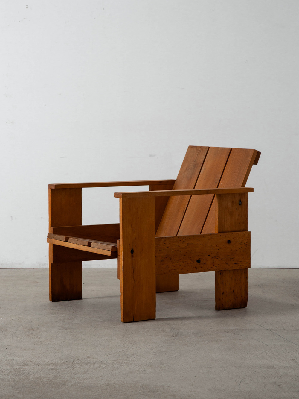 ‘Crate’ Lounge Chair by Gerrit Thomas Rietveld for Cassina in Pine
Netherlands , 1980s
オランダ人デザイナー・建築家の Gerrit Thomas Rietveld （ヘーリット・トーマス・リートフェルト）によって1934年にデザインされた ‘Crate’ チェア。家具輸送に使われる木箱（Crate）から着想を得て生まれたシリーズ「Crate Furniture」のひとつ。
木箱に多用されるパイン材を使用し、真鍮ビスで組み立てるシンプルな構造が特徴で、購入者自身が一から組み立てを行うDIYキットとして販売されました。その合理的で質素な佇まいは、一部の評論家から「クラフトの腐敗」とも揶揄されましたが、リートフェルトは次のように応じています。
「上質な木材で丁寧に作られた家具は、傷や破損から守るために木箱に入れて出荷される。この木箱は、その高貴な家具よりも丈夫。さらに陽気な色合いで、職人のしかめっ面を感じさせない。だからこそ、最終的に ‘家具’よりも‘木箱’を選んだ人がいたはずだ」
こちらの個体はイタリア Cassina（カッシーナ）社製となり、座面裏面には当時の刻印と製造番号が刻まれています。
