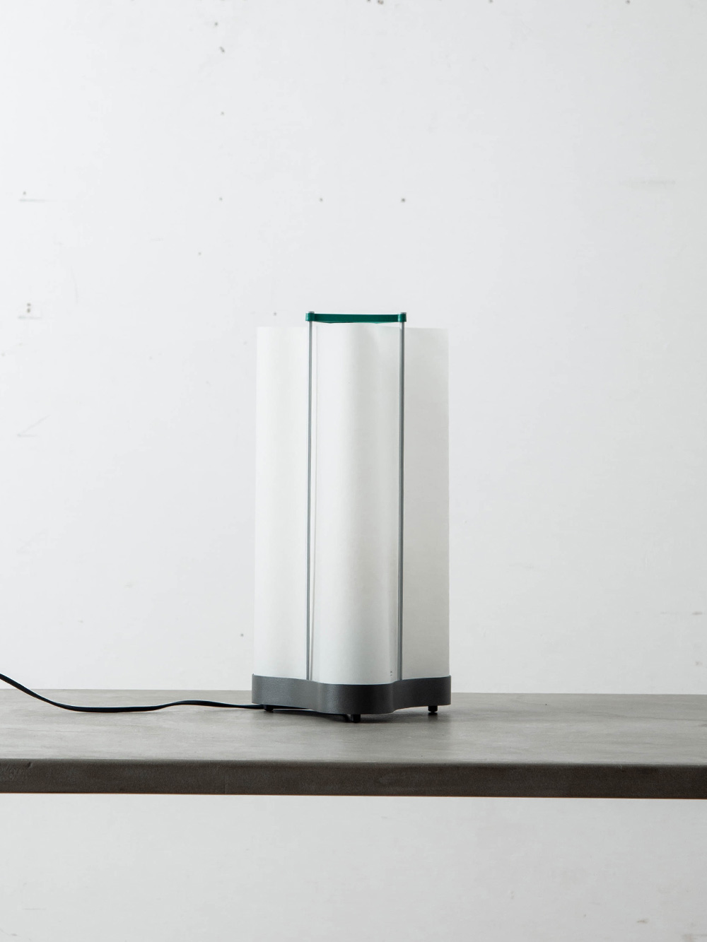 Lampe Cabanon Table Lamp by Le Corbusier for NEMO
Italy , 1950s
ル・コルビュジエは1952年、フランス南部の海岸沿いに小さな小屋「キャバノン」を建設しました。
広さはわずか14㎡ほどで、最小限の空間で本質を追求した、暮らしの原型ともいえる建築です。
彼が考案した人体比例理論「モデュロール」に基づいた設計で、晩年の住まいとして使われました。
Lampe Cabanon（ランプ・キャバノン） は、「カップ・マルタンの休暇小屋」とも呼ばれたこの小屋にちなんで名付けられ、本質的な暮らしの象徴となっています。
シェードには彼が愛用していたトレーシングペーパーを用い、第二次世界大戦中に使用された迫撃砲の弾薬運搬ケースを素材として再利用しました。
このケースはフランスの海岸で発見されたものでした。
多数のスケッチや設計図が残るこのランプは、戦後の「再生」を体現し、建築・デザイン・暮らしの本質を結びつけた象徴的なプロダクトです。
