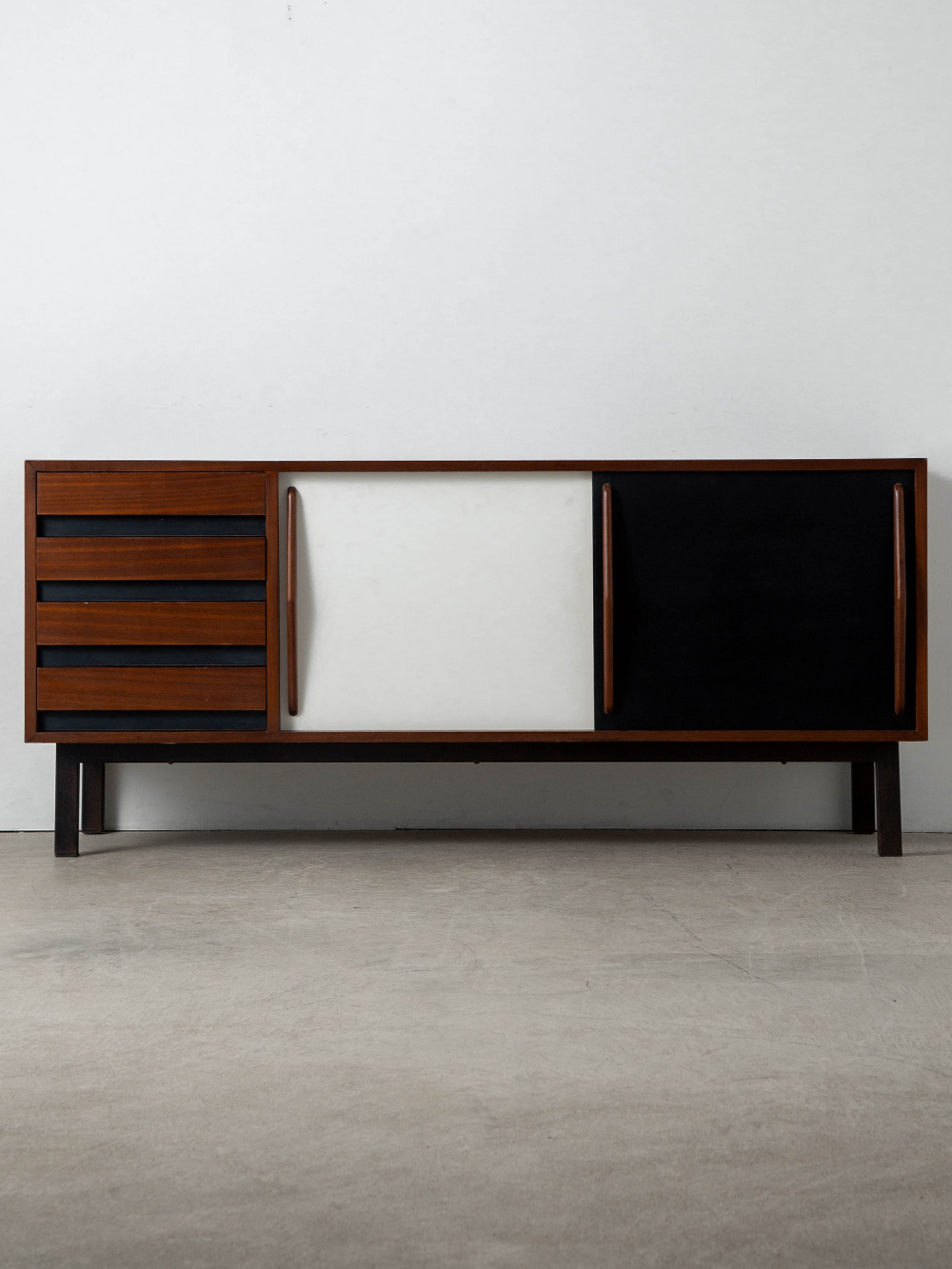Sideboard by Charlotte Perriand for Steph Simon in Ash and Steel
France , 1950s
フランスの建築家・デザイナーである Charlotte Perriand（シャルロット・ペリアン）によって、西アフリカ、モーリタニアの旧鉱山都市 Cansado（カンサド）の住居および宿泊施設のために、1958年にデザインされたサイドボード。彼女の長年のディーラーであった、Steph Simon（ステフ・シモン）によってエディション化されました。
マホガニー材の突き板を施した構造、鮮やかな白と黒のコントラストが際立つ2枚の引き戸が特徴で、収納力を最大限に高める4つの横引き引き出しを備えています。黒漆塗りの金属製ベースによって持ち上げられたこの作品は、重厚感と視覚的な軽やかさの完璧なバランスを実現し、機能的な優雅さとミニマルデザインの真髄、当時のモダニズムの精神を体現しています。
収納は実用的要素のみならず生活空間に調和と明瞭さをもたらす手段の一つと捉え「空虚を創造する」というマントラを基にプロダクトに反映。木製構造と工業的な脚部に黒と白のラミネート引き戸により空間に上品さを演出する、時代を超越したデザインです。 1956-1974にかけてSteph Simon（ステフ・シモン）によって製造された個体となります。
