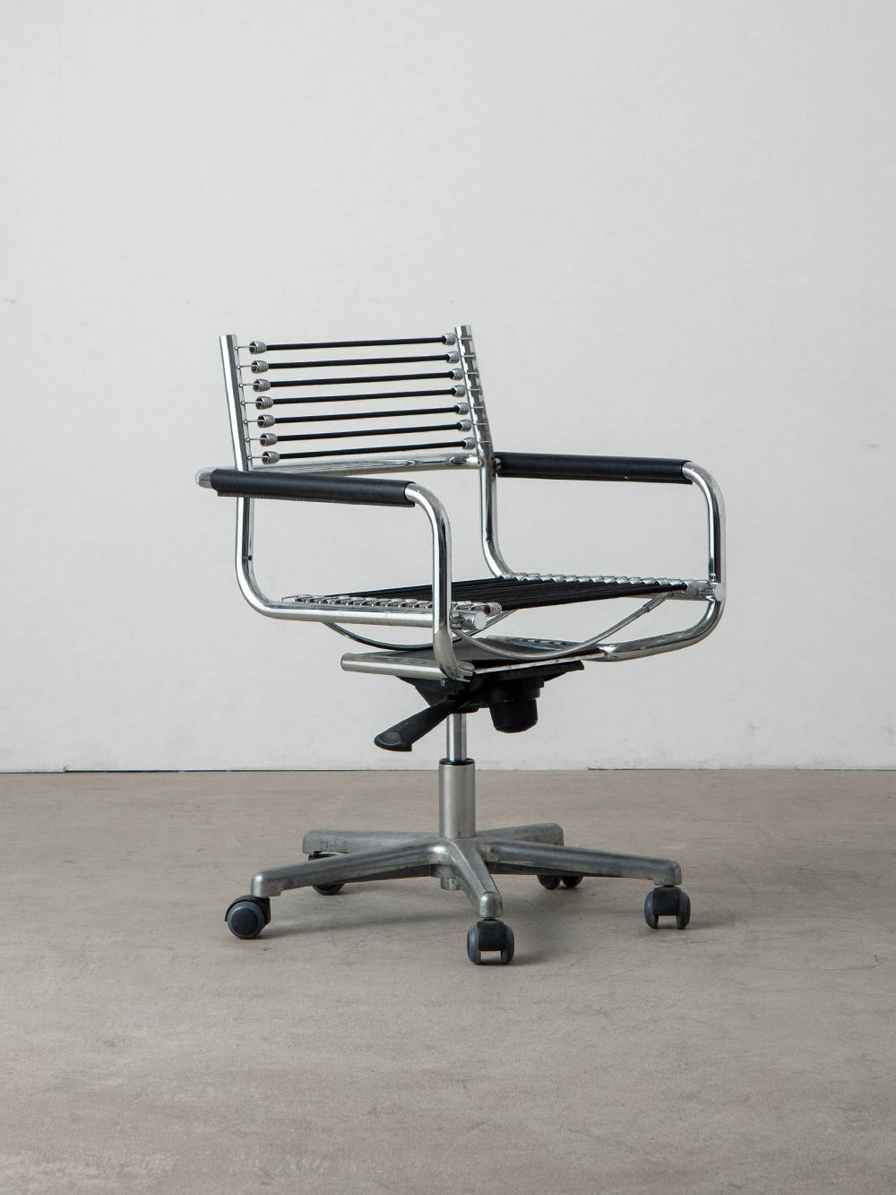 Sandows Office Chair by René Herbst for Ecart International in Chrome and Elastic cord
Italy , 1980s
フランスの建築家・デザイナー René Herbst（ルネ・エルブスト）によってデザインされた Sandows（サンドウズ）オフィスチェア。
ミニマルなクロームメッキのフレームと、抜け感のあるエラスティックコードの調和が美しいチェア。
装飾的な布張り家具が主流だった時代に、弾力のある工業用コードを張り巡らせることで身体を支えるという、当時の常識を覆す革新的な着想から生まれた作品です。
こちらの個体はキャスター付きのオフィスチェアで、80年代の Ecart International（エカール・インターナショナル）製と推定されます。
