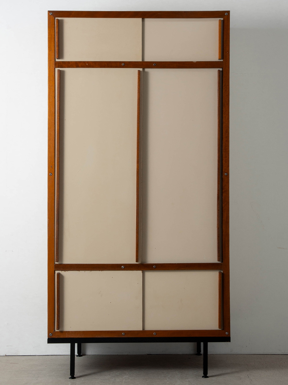 Cabinet by André Sornay in Mahogany and Steel
France , 1960s
フランス人デザイナー André Sornay（アンドレ・ソルネ）によってデザインされたキャビネット。
深みのあるマホガニーとオフホワイトのコントラストが美しく、ソルネが考案しフランス国内外で特許を取得した Tigette System が用いられています。Tigette はフランス語で「小さなロッド」を意味し、金属ロッドによって全てのパーツを組み立て・分解することができるこの構造は、戦後復興期に広がったモジュール家具に対するソルネ独自のアプローチとして生み出されました。
当時のフランスのモジュール家具では、接合部を内部に隠すことが主流でしたが、ソルネはあえて外部に露出させ、構造をデザインの一部として取り込んでいます。この Tigette System は、1950-70年代の彼の作品群を象徴するシステムであり、後のノックダウン式家具の発展にも大きな影響を与えています。
また、端正に現れるマホガニーのフレームと取手が縦横のラインを明確に際立たせ、その連続性が美しいグリッド・コンポジションを形成。スチール脚が空間に軽やかな抜けをもたらし、全体の構成をより明快に引き立てています

