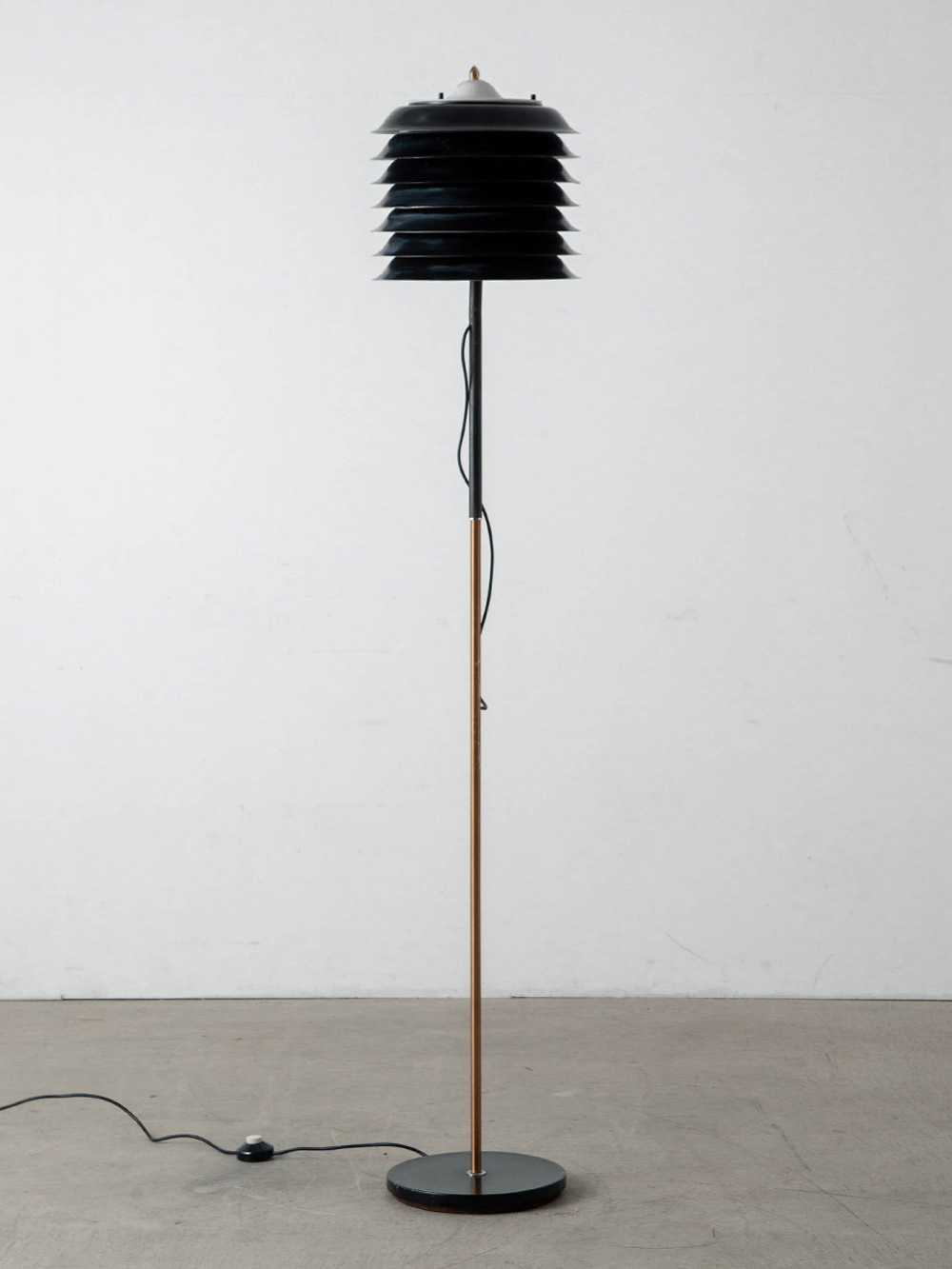 Floor Lamp for STILNOVO in Steel , Brass and Marble
Italy , 1960s
イタリアより、建築的なフォルムと洗練された佇まいが美しいフロアランプ。
水平に重ねられたシェードの連続性は非常に構築的で、細身の支柱との対比が際立ち、空間に静かな存在感をもたらします。 点灯時には、シェードの輪郭が柔らかく浮かび上がり、光源を覆い隠しながら穏やかな反射光を拡散。直接的な眩しさを抑えつつ、空間に落ち着いた陰影と奥行きを生み出します。
こちらは、イタリア・ミッドセンチュリー期を代表する照明メーカー STILNOVO（スティルノボ）社によるもの。同社は Ettore Sottsass（エットレ・ソットサス）や Joe Colombo（ジョエ・コロンボ）といった、20世紀イタリアデザインを象徴するデザイナーたちとの協業でも知られています。
素材使い、光のコントロール、そして造形美。そのいずれにも、当時のスティルノボ社が誇った高い技術力とデザイン思想が息づいています。
