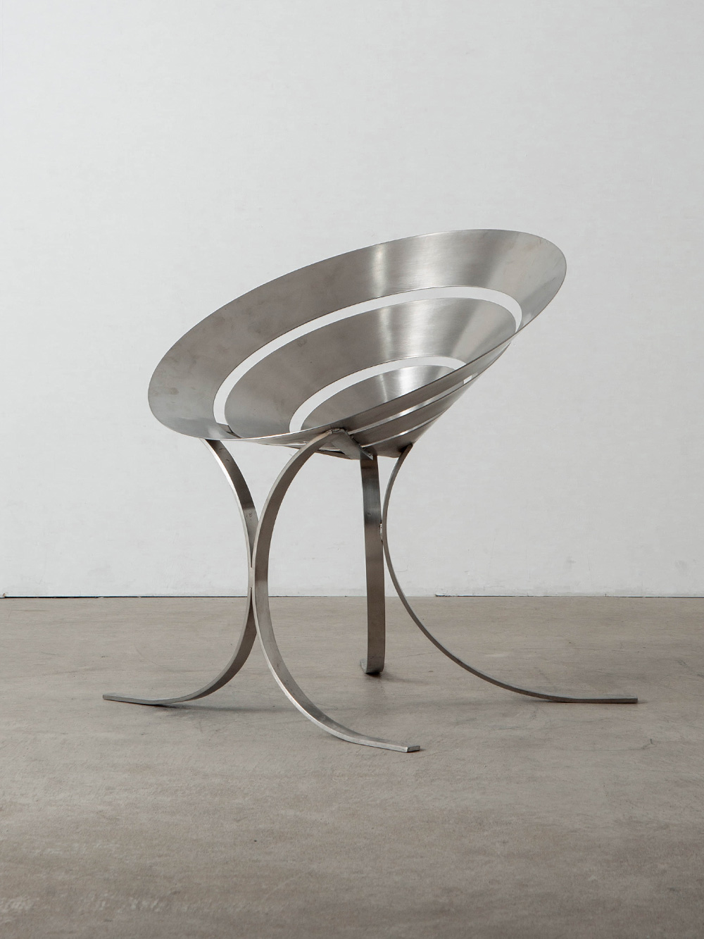 Ring Chair by Maria Pergay for Ugine-Gueugnon in Stainless Steel
France , 1960s
フランス人デザイナーの Maria Pergay（マリア・ペルゲイ）によって、同国の Ugine-Gueugnon（ユージン・グーニョン）社のために、1968年にデザインされた Ring（リング）チェア。
オレンジの皮を剥く様子からデザインの着想を得たとされ、彼女を象徴する素材であるステンレススチールとの調和が美しいプロダクトです。
かのピエール・カルダンにも愛され、パリのギャラリーでペルゲイ初のステンレス家具コレクションを見たカルダンは、そのすべてを買い上げたとも言われています。後に自身のブティックの什器
