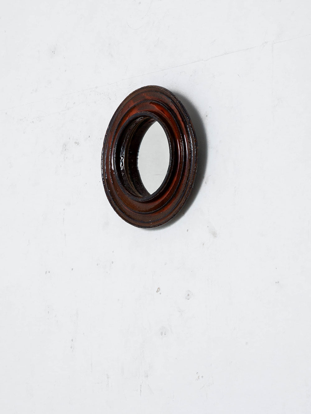 Mirror by Gérard Hofmann for VALLAURIS in Glass and Ceramic
France , 1960s
フランス人陶芸家 Gérard Hofmann（ジェラール・ホフマン）によって、古くから陶器の産地として知られる、南仏　コート・ダジュール近くの村 VALLAURIS（ヴァロリス）で製作されたウォールミラー。
ヴァロリス陶芸を象徴する彫刻的な造形。同心円状に成形したセラミックフレームに、深みのある赤褐色の釉薬を施し、豊かな立体感と陰影を生み出しています。
