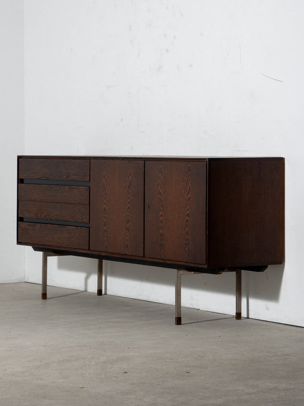 Sideboard by Rudolf Bernd Glatzel for Fristho Franeker in Wenge and Steel
Netherlands , 1960s
ドイツのデザイナー Rudolf Bernd Glatzel（ルドルフ・ベルント・グラッツェル）によって、オランダの家具メーカー Fristho Franeker（フリスト・フラネケル）社のためにデザインされたサイドボード。
ウェンジ材による重厚な木部に、直線的な金属フレームを組み合わせた構成で、木材の重厚感と軽やかな脚部とのコントラストが特徴です。
内部には Pastoe（パストー）社のラベルが残されており、Fristho社の家具を取り扱っていたことが推測されます。
