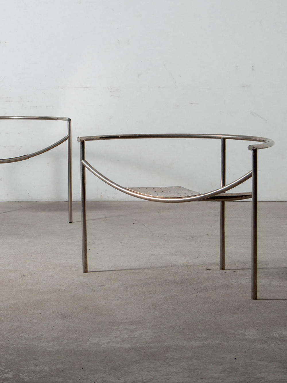 Dr. Sonderbar Chair by Philippe Starck for XO in Steel
France , 1980s
フランス人建築家・デザイナーの Philippe Starck（フィリップ・スタルク）によって、フランスの XO社の為に1983年にデザインされた Dr. Sonderbar チェア。
チューブラースチールによる三脚構造とパンチングメタルの座面が特徴的な、軽やかで洗練されたデザイン。
「第四の脚は冗長である。三脚は緊張感を生む。三本脚の座面は異なる精神性を持つ。それは座る人により多くの注意、より大きな参加、そして知的かつ感覚的な要求を求める。三脚で揺れることは危険だが、より楽しい。」と述べいています。
名称はフィリップ・K・ディックの小説「Ubik（ユービック）」に登場するゾンダーバー博士に由来。
スタルクは、60点近くに及ぶ初期作品で同様に小説の登場人物や場所の名前を用い、デザインに物語性を添えています。
80年代を象徴するこのチェアは、人々のデザインへの関心を再び呼び起こすことを目的とした、スタルクの「社会的に認知される家具をより多くの人に普及させる」という思想を反映しています。
